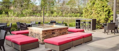 An outdoor patio with a stone fire pit, wicker furniture, and a view of a lake.