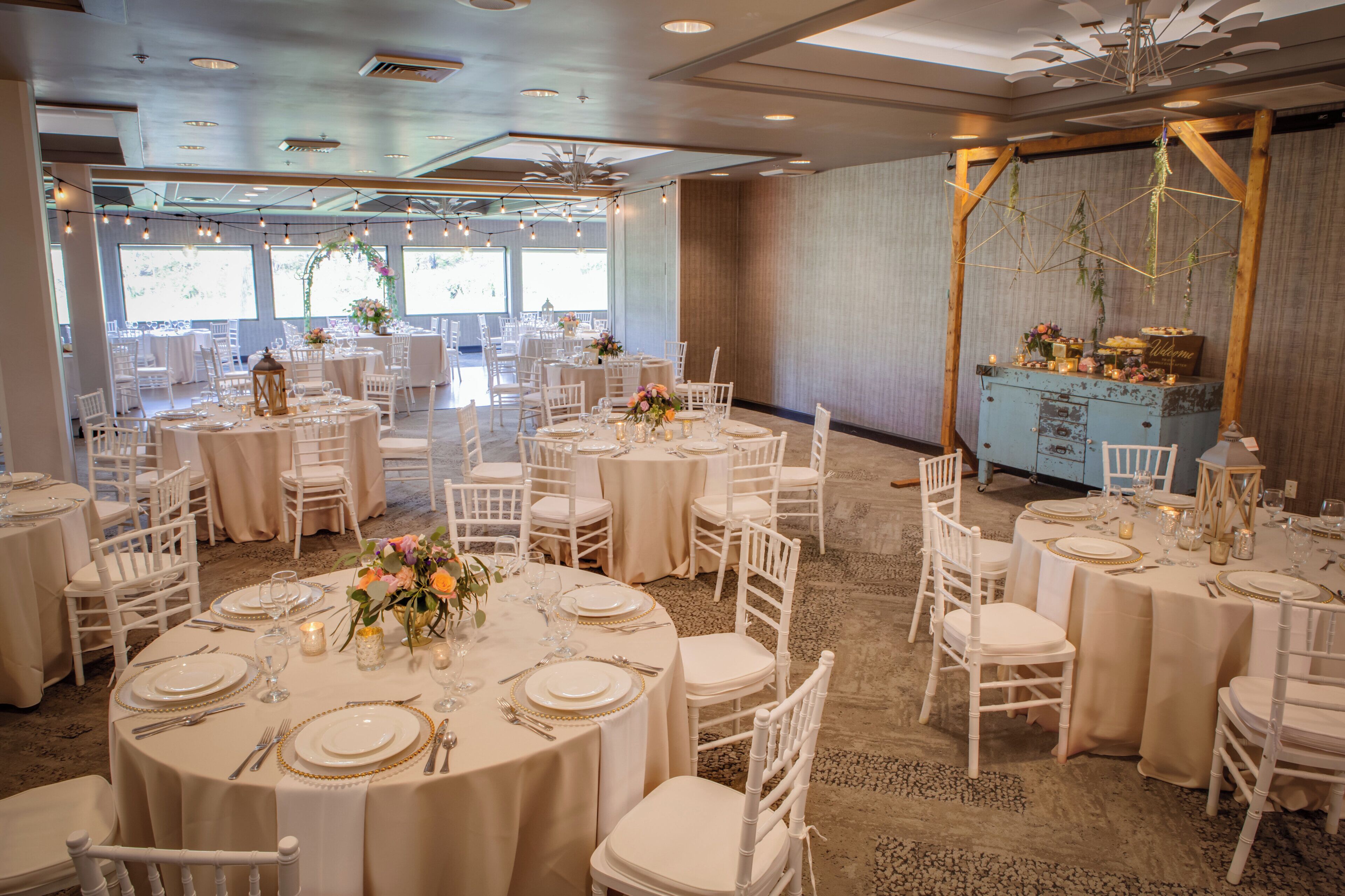 A banquet hall with round tables, white chairs, and a buffet area.
