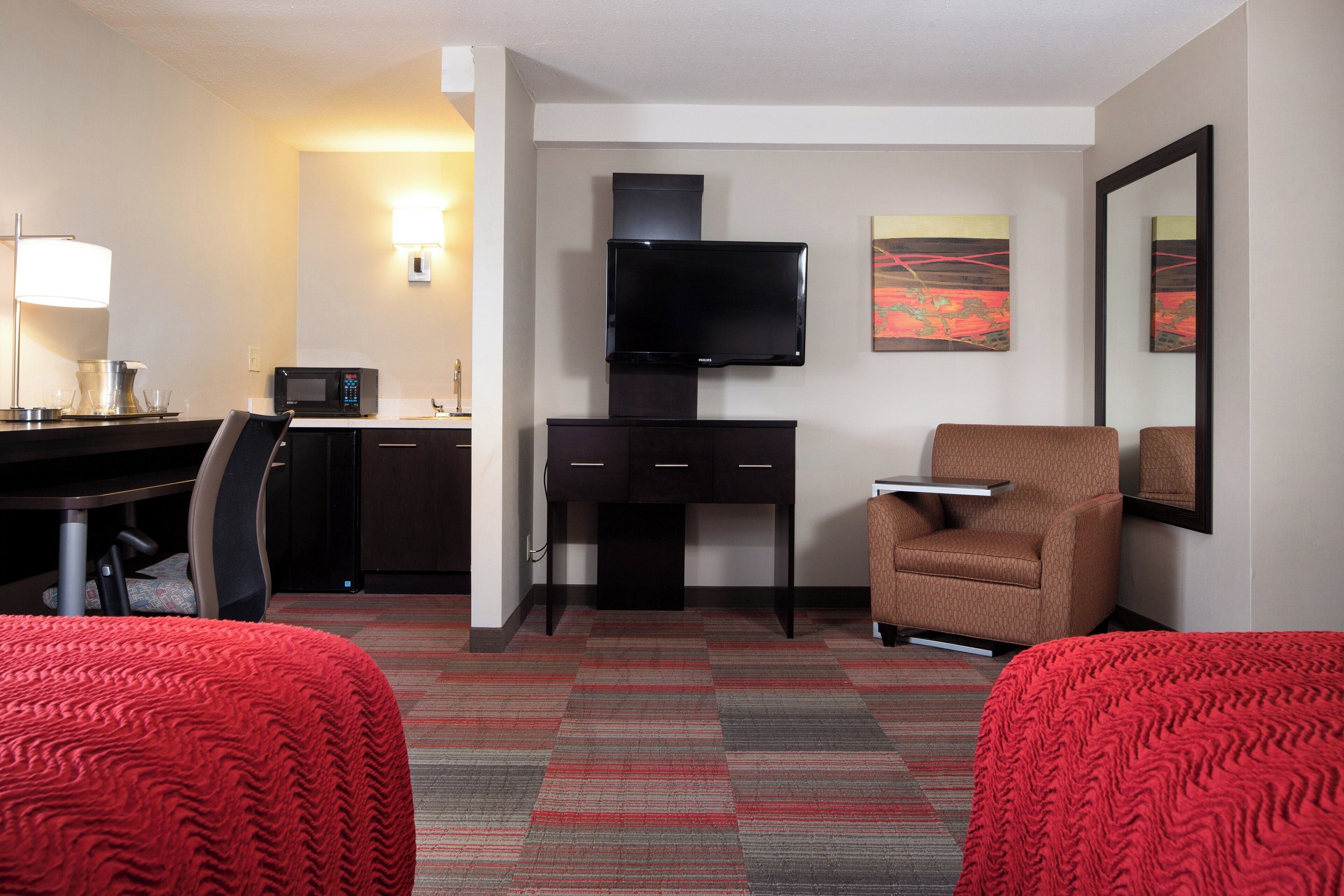 Una habitación de hotel con escritorio, televisión de pantalla plana, silla, cama y piso alfombrado.