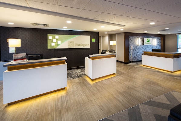 A Holiday Inn reception area with two reception desks, a large screen displaying the Holiday Inn logo, and a patterned carpet. - Holiday Inn Milwaukee Riverfront by IHG (Milwaukee)