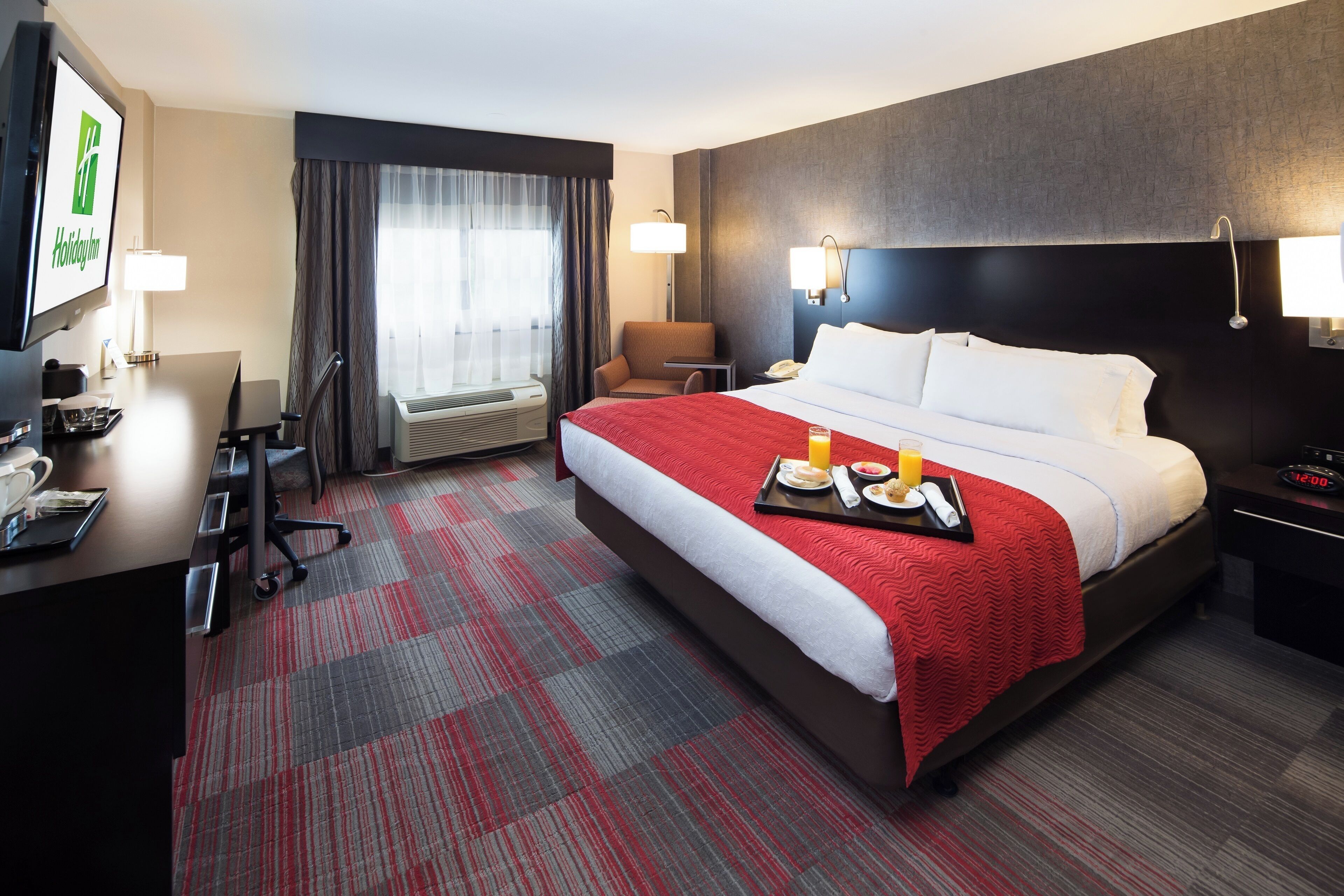Une chambre d’hôtel avec un lit, un bureau, une chaise, une télévision et une fenêtre avec des rideaux.