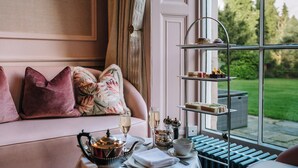 Un rincón acogedor con una mesa preparada para el té, una bandeja escalonada de postres y vistas al jardín.