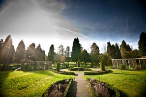 A well-maintained garden with a central pathway, surrounded by neatly trimmed hedges and tall trees. - Champneys Mottram Hall (Macclesfield)