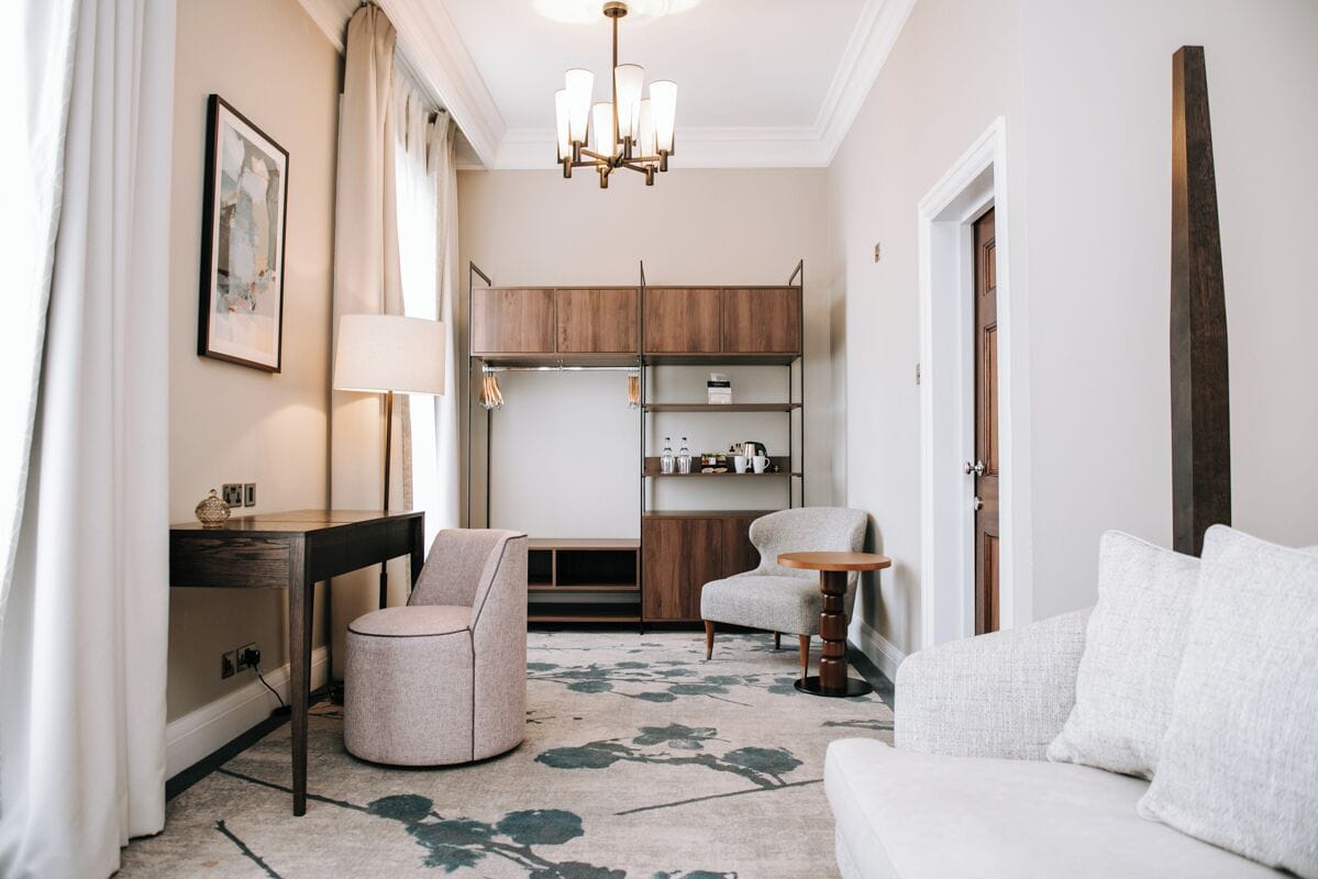 Une chambre d’hôtel moderne comprenant un canapé, un fauteuil rond, un bureau, une lampe, un lustre, une armoire et une petite table.