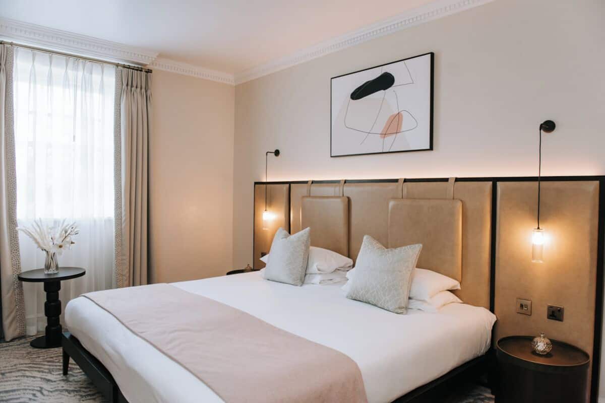 A hotel room with a large bed, a bedside table with a vase, and a wall-mounted artwork.