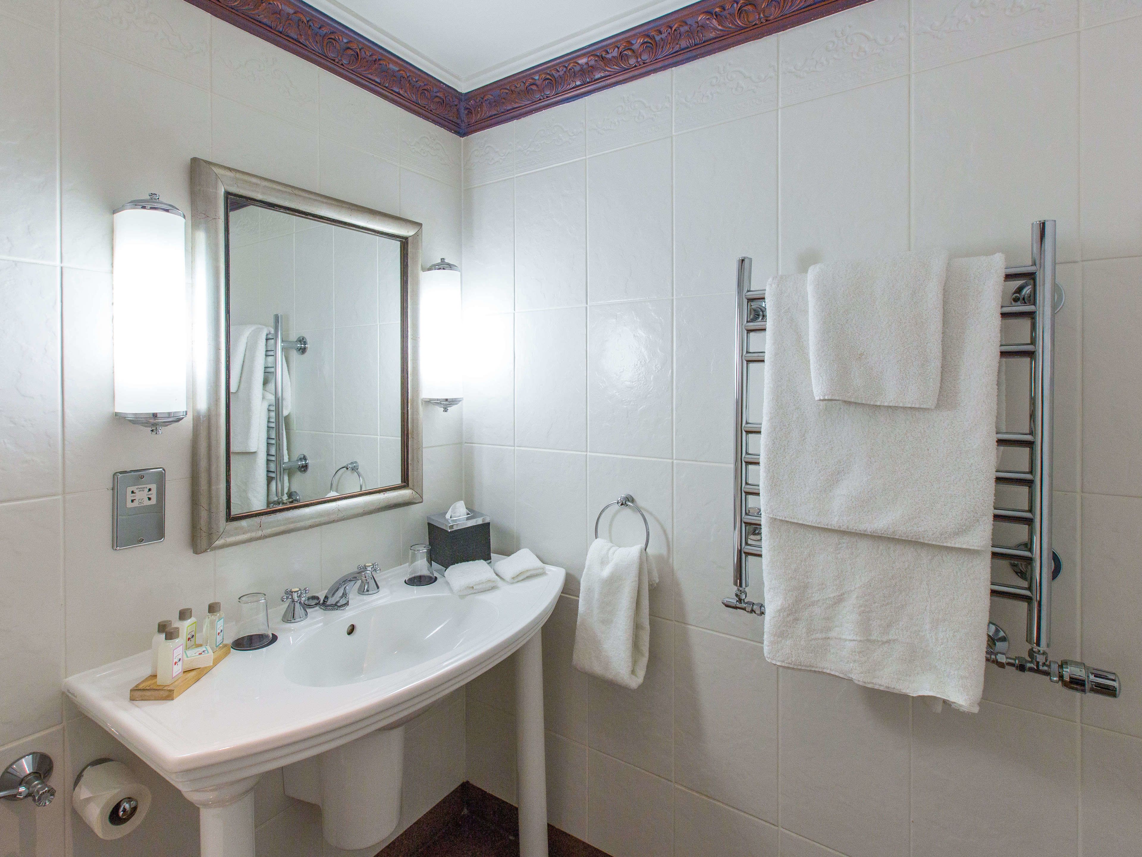 Ein Badezimmer mit einem weißen Waschbecken, einem Spiegel, einem Handtuchhalter und einem Toilettenpapierhalter.