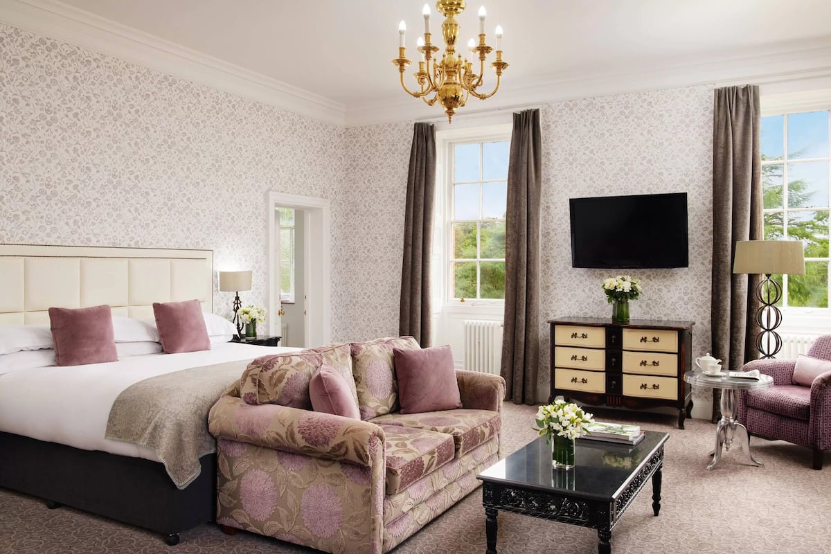 A hotel room with a large bed, a sofa, a coffee table, a TV, and a dresser.