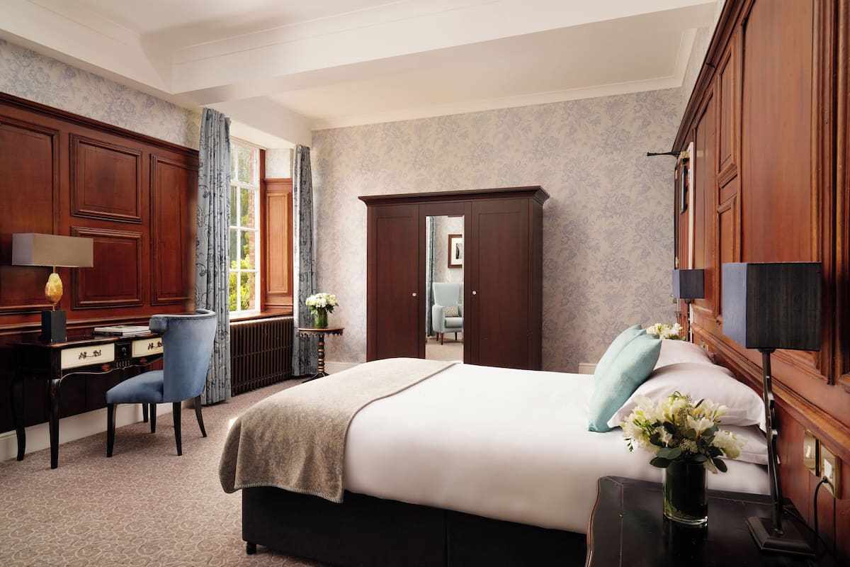 A hotel room with a large bed, a desk with a chair, a wardrobe, and a view of the outdoors.