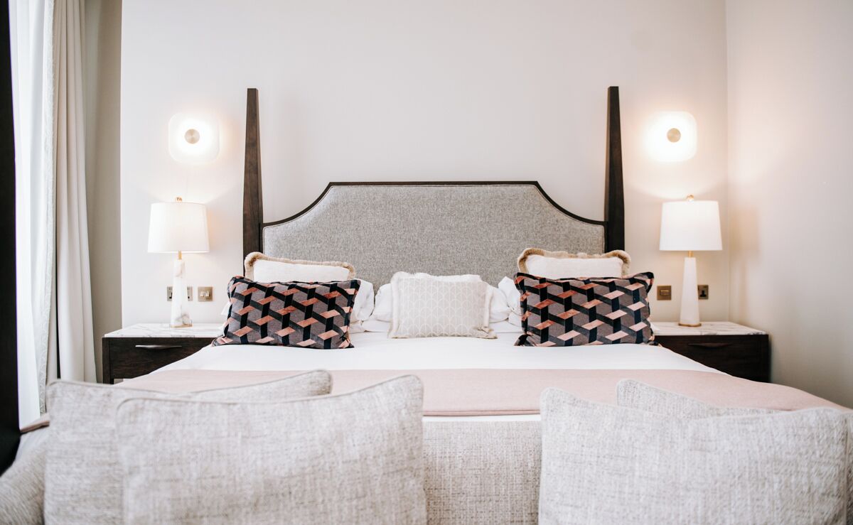 A neatly arranged hotel room with a large bed, two bedside tables with lamps, and a headboard with a light fixture.