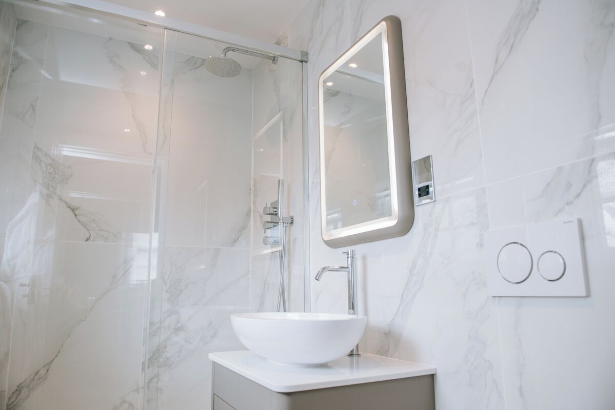 Une salle de bain moderne avec un lavabo en marbre blanc, une douche en verre et un miroir fixé au mur.