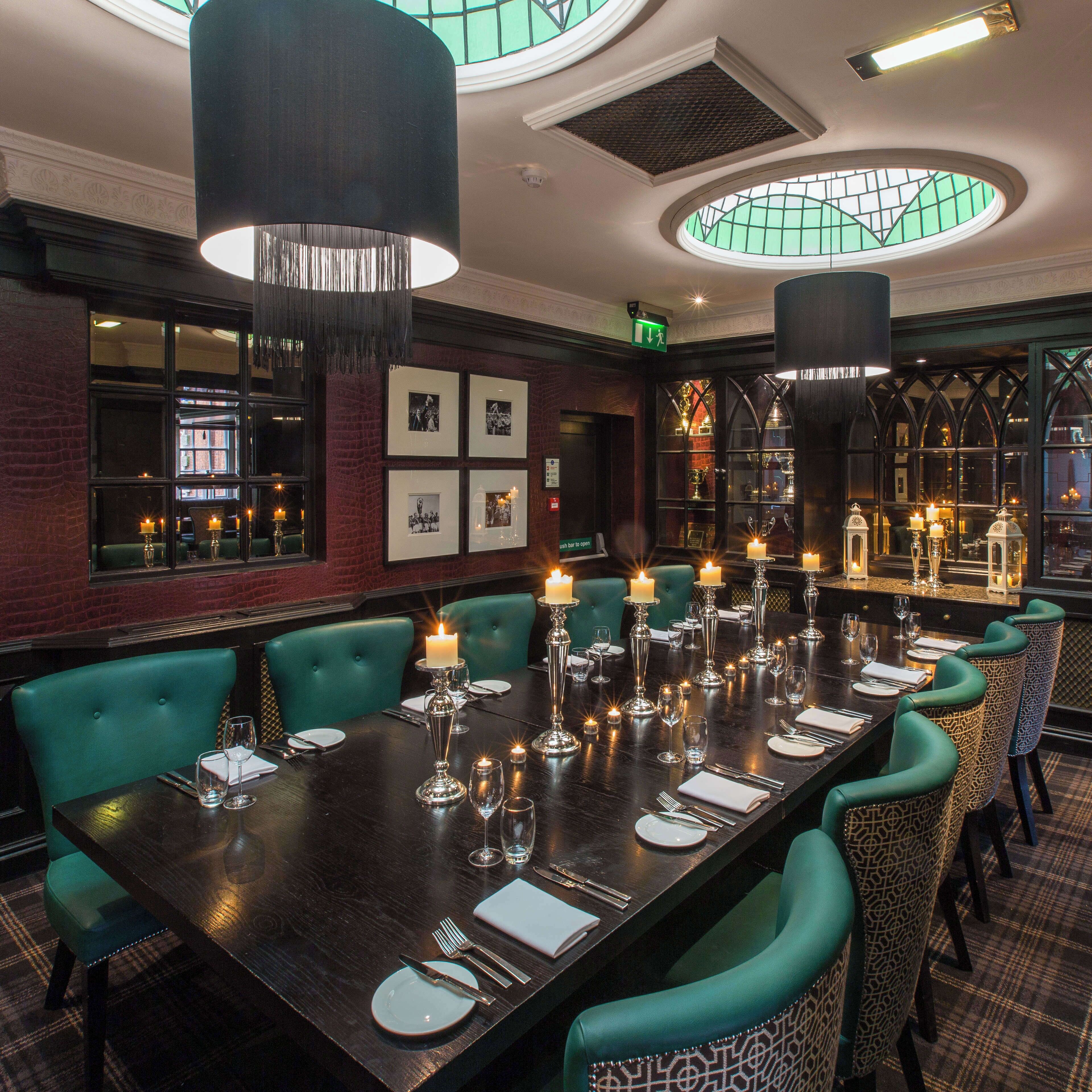 A long dining table set for a meal with candles, surrounded by green upholstered chairs.
