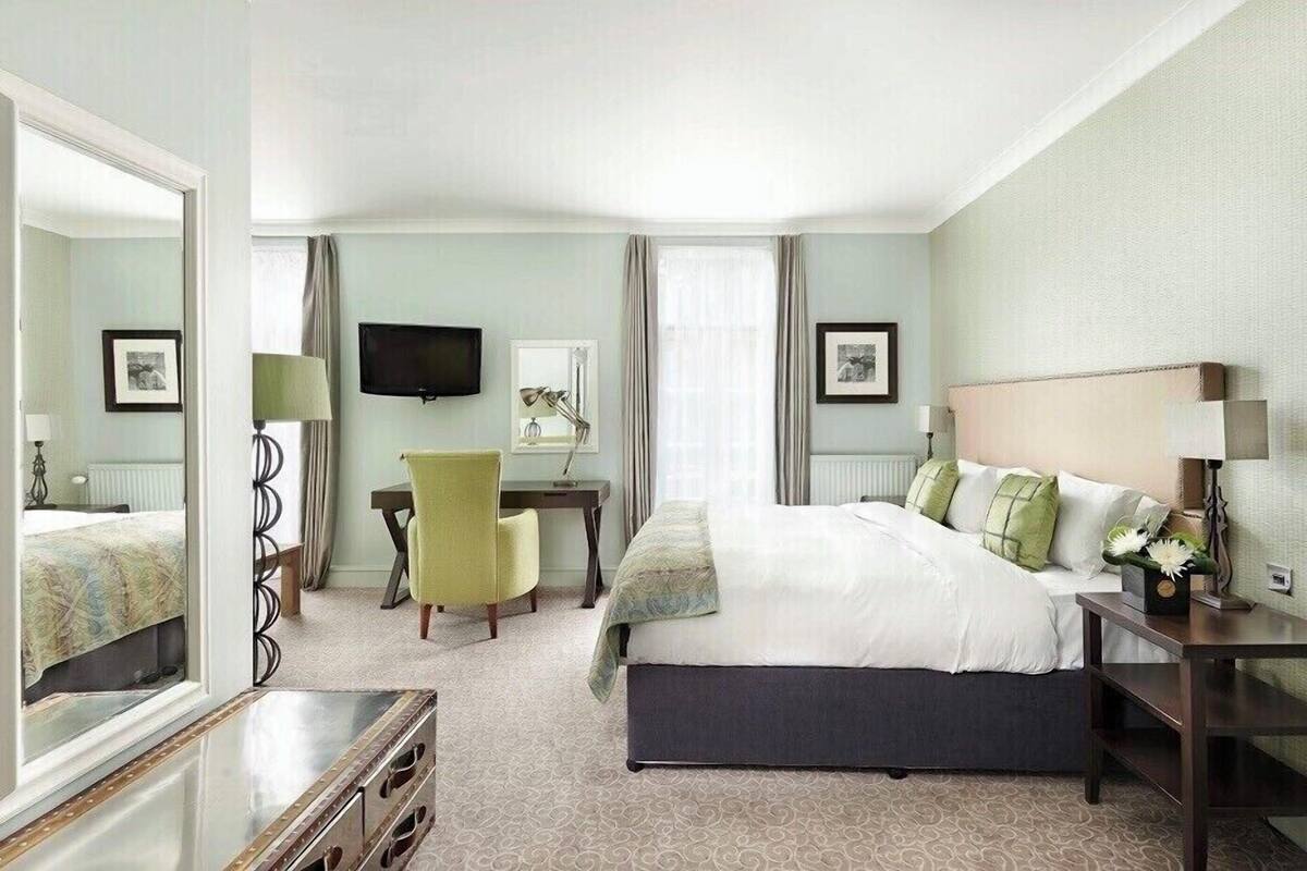A hotel room with a bed, a desk, a chair, a TV, and a mirror.
