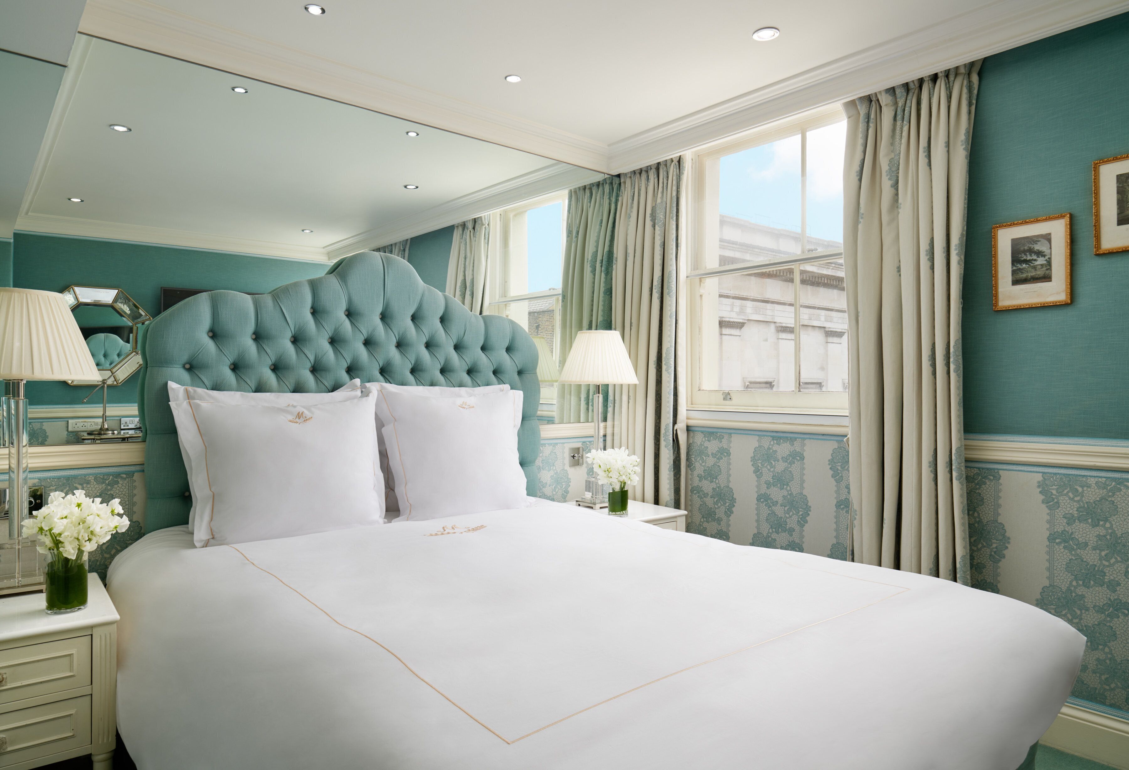 A large bed with a tufted headboard, white bedding, and two bedside tables with lamps and vases of flowers.