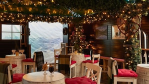 Un interior acogedor con muebles de madera rústica, un árbol de Navidad y vistas a montañas nevadas a través de un amplio ventanal.