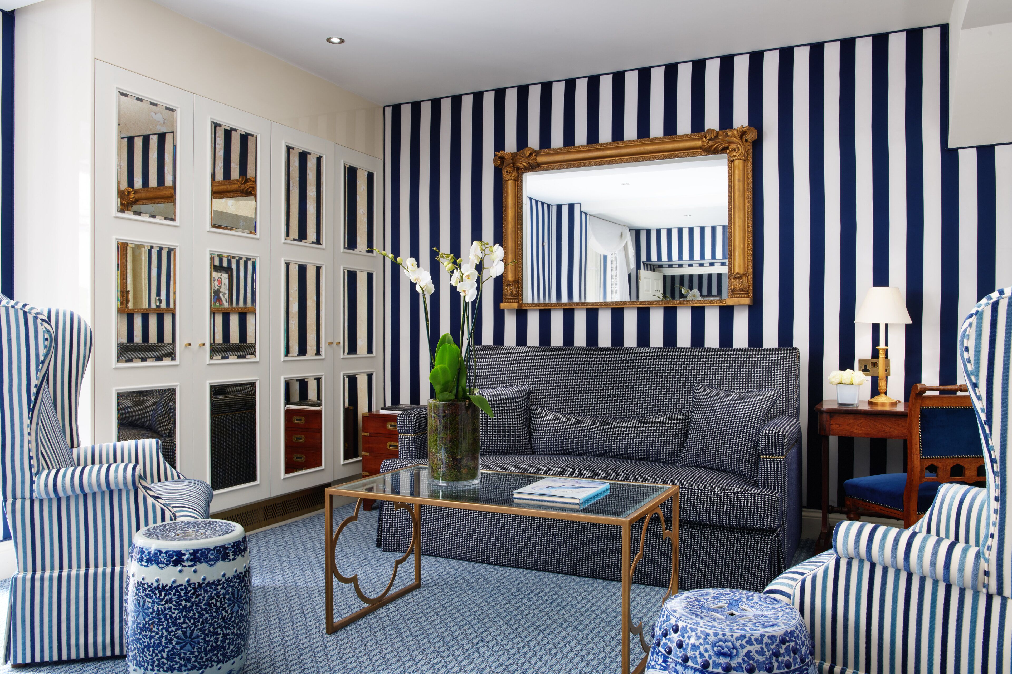 A room with striped wallpaper, a sofa, armchairs, a coffee table, and a mirror.