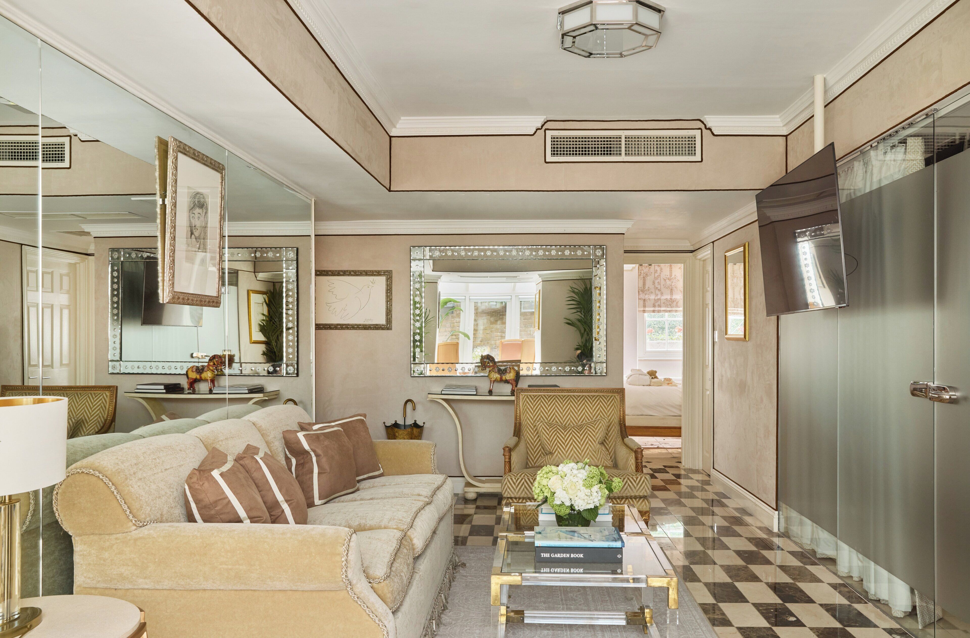 A well-lit living room with a checkered floor, a sofa, a coffee table with books, and a large mirror.
