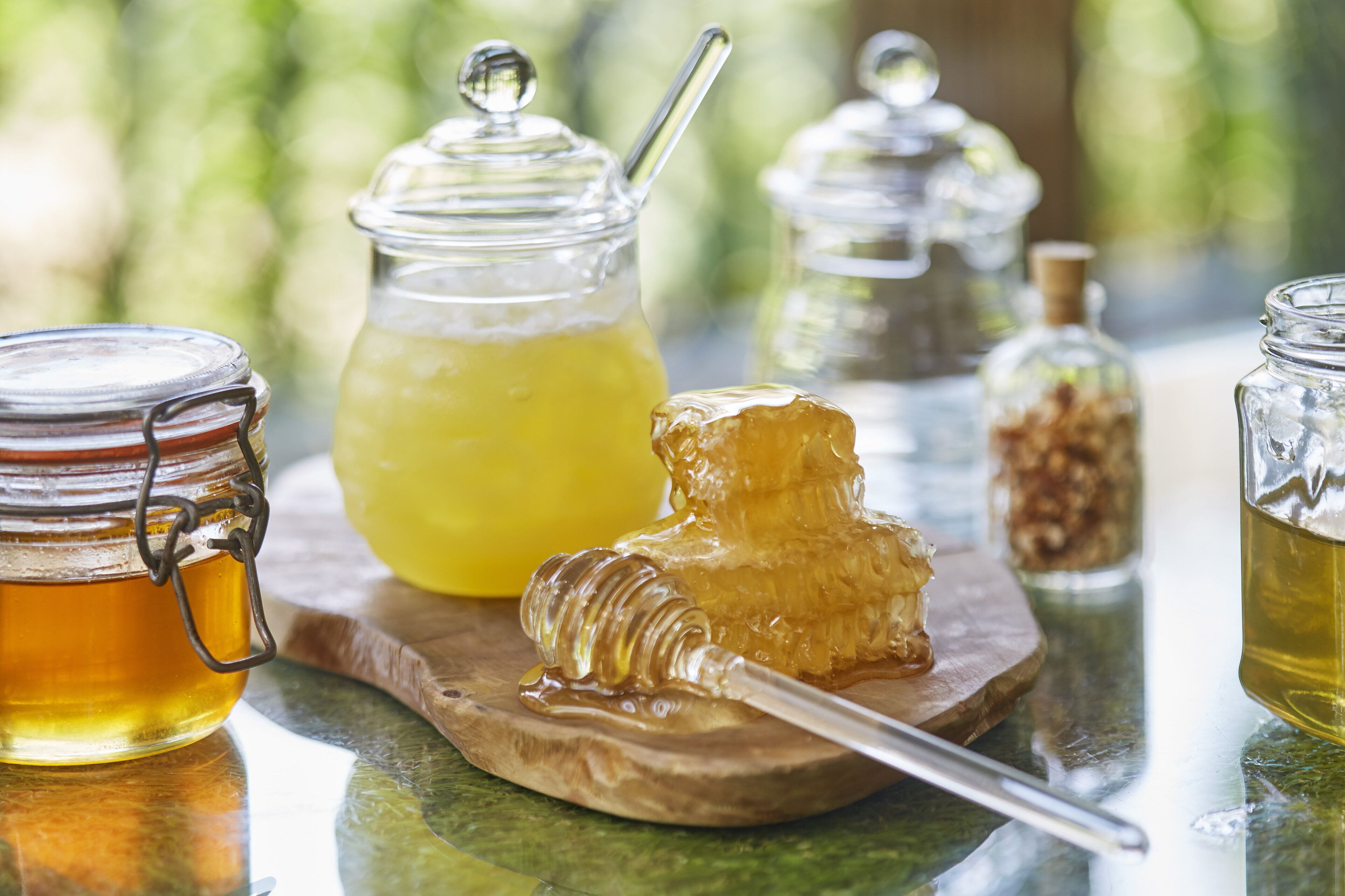 A wooden board with jars of honey and honey dipper.