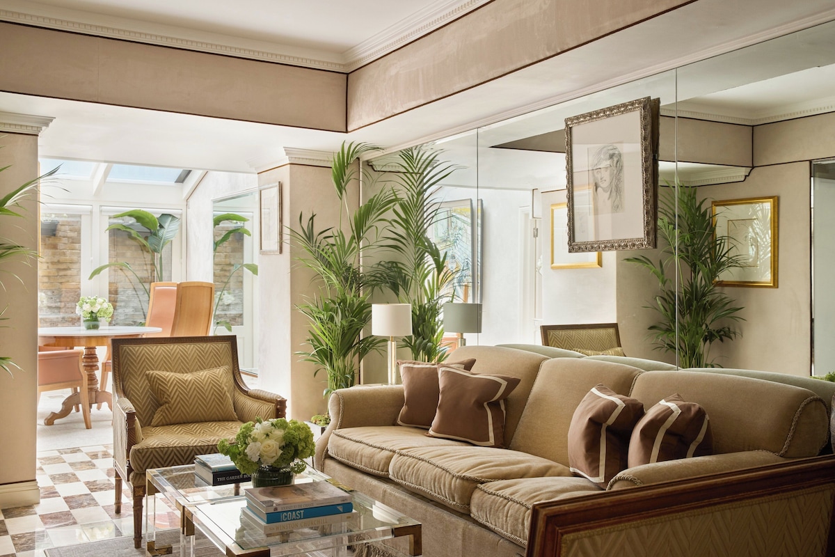 Un salón con un sofá color beige, sillones, una mesa baja con libros y plantas en macetas.