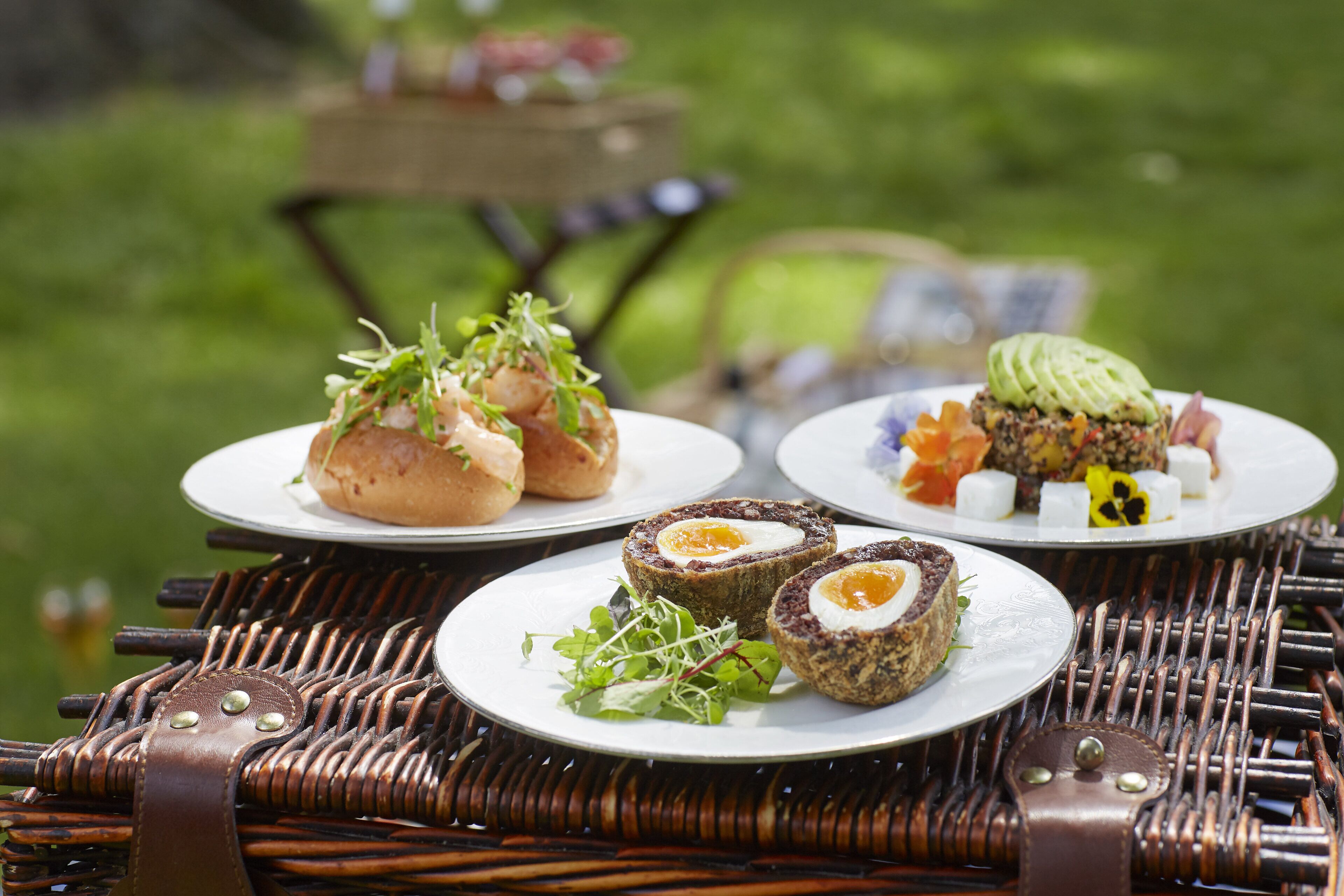A wicker table with plates of food, including meat pies and a dish with avocado.