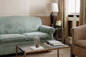 Ein Wohnzimmer mit einem grünen Sofa, einem Glastisch mit Büchern, einer Lampe und einer Vase mit Blumen.