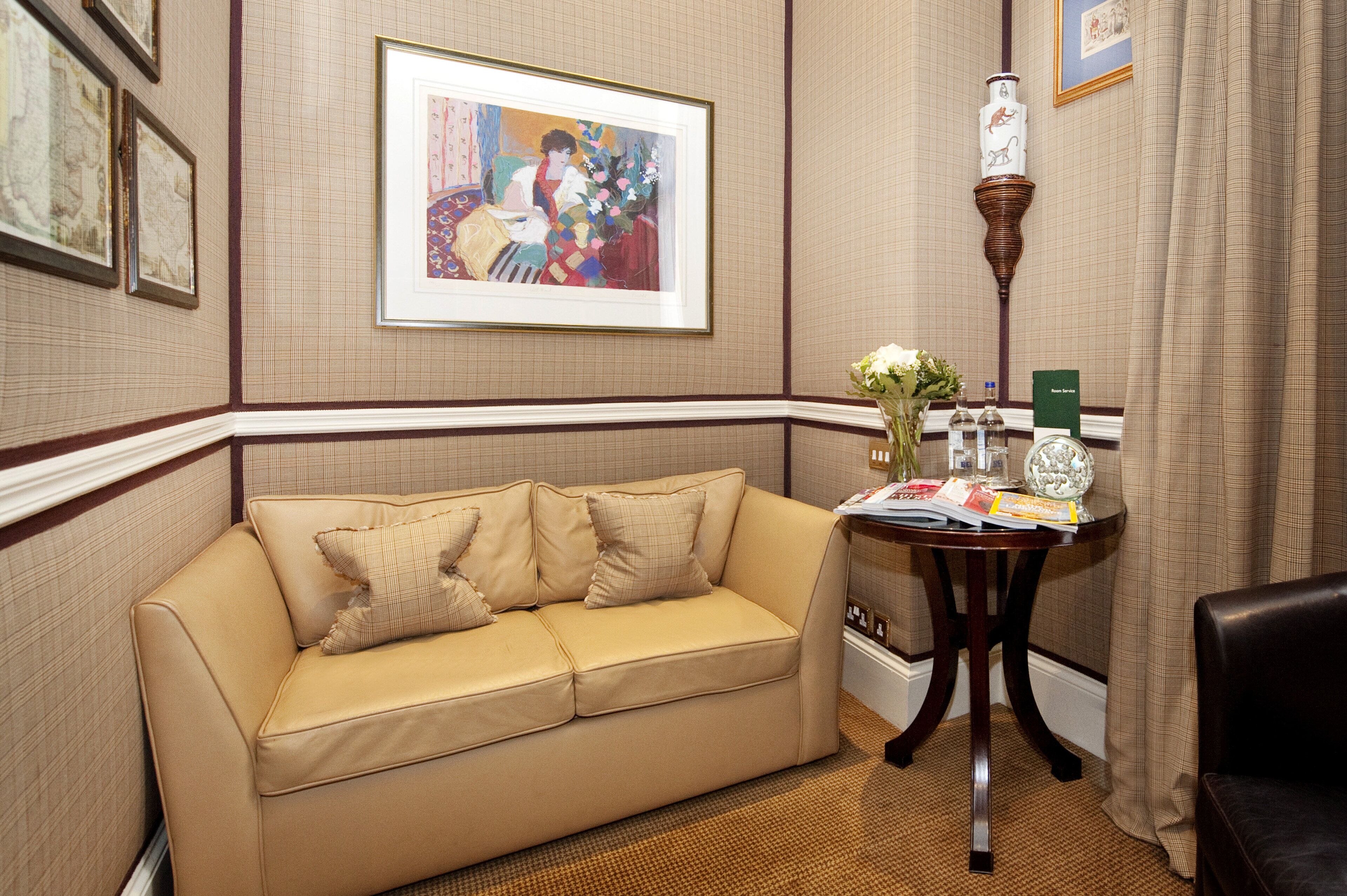 A beige sofa with pillows, a small table with a vase of flowers, and framed artwork on the wall.