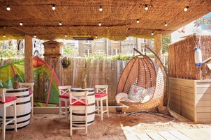 An outdoor seating area with striped chairs and a hanging chair, surrounded by a wooden fence and a thatched roof.