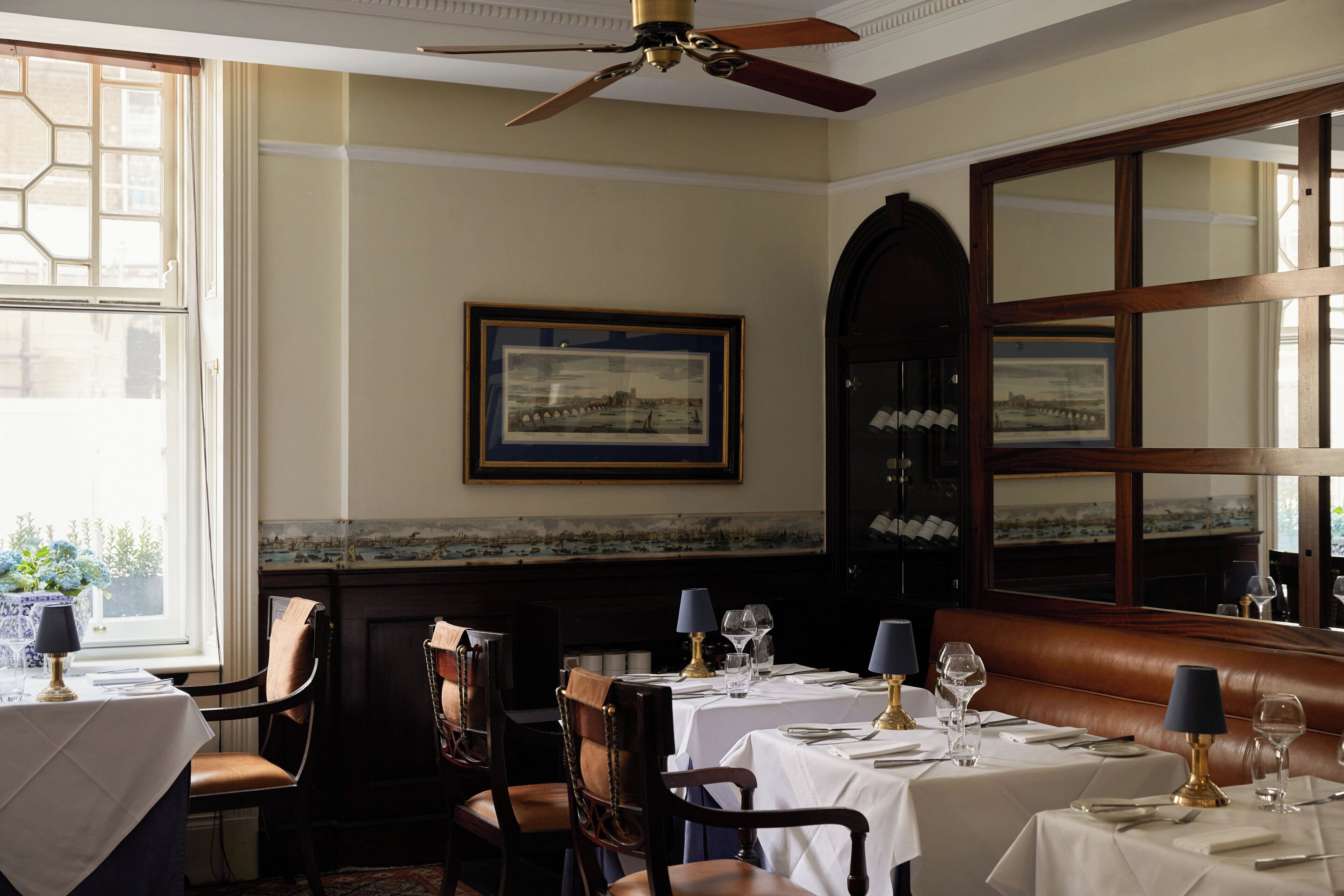 A dining area with tables set for two, chairs, a ceiling fan, and a large mirror on the wall.