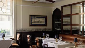 A dining area with tables set for two, chairs, a ceiling fan, and a large mirror on the wall.