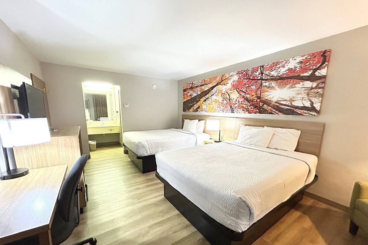 A hotel room with two beds, a desk, a chair, a desk lamp, and a large painting on the wall.