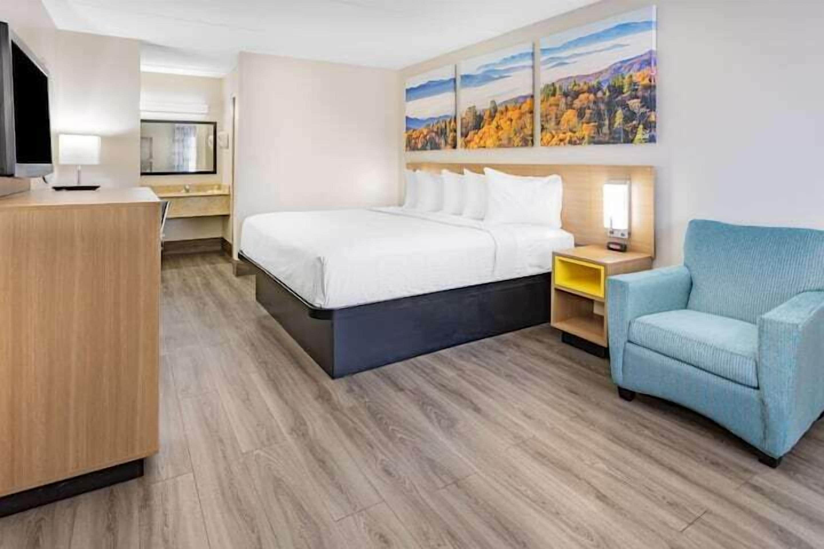 A hotel room with a large bed, a desk with a TV, a chair, and a painting on the wall.