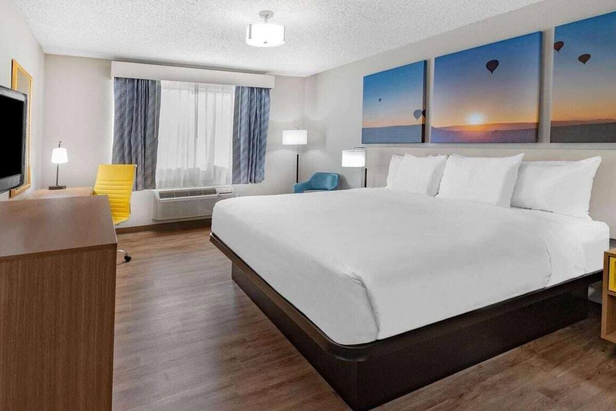 A hotel room with a large bed, a TV, a desk, and a window with curtains.
