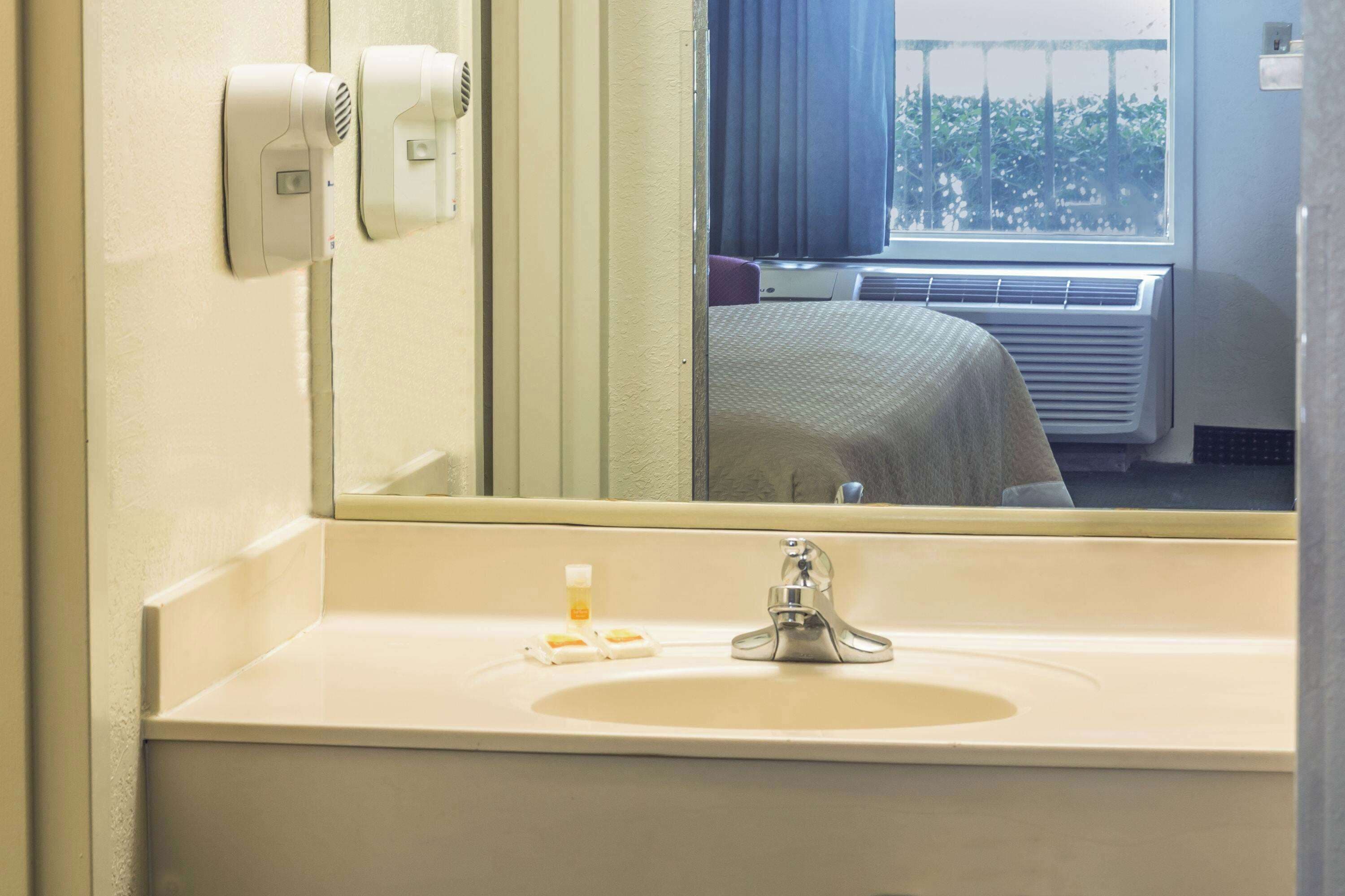 A hotel bathroom with a sink, mirror, and window.