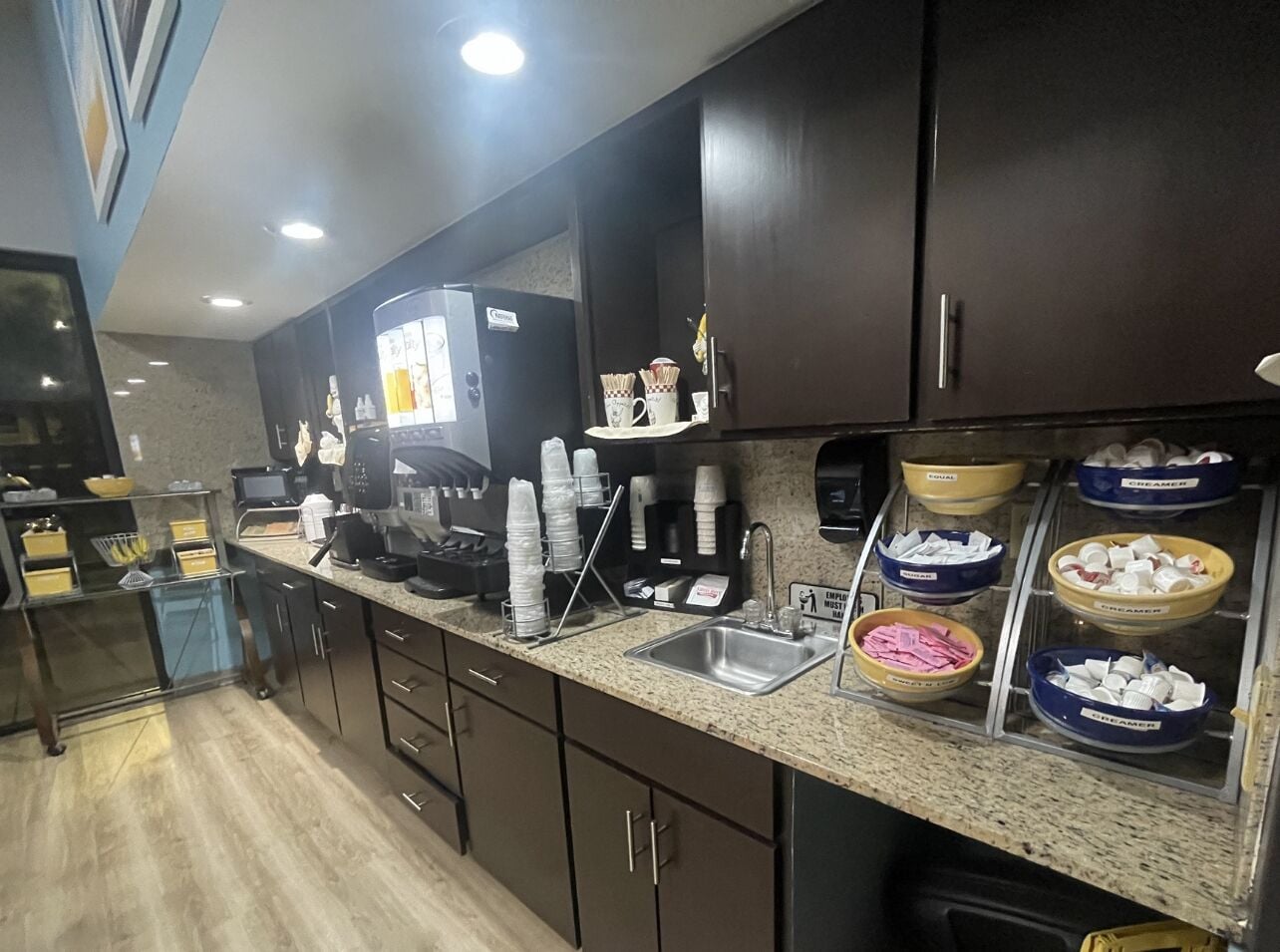 Una cocina con estación de café, un lavamanos y diferentes recipientes para alimentos.