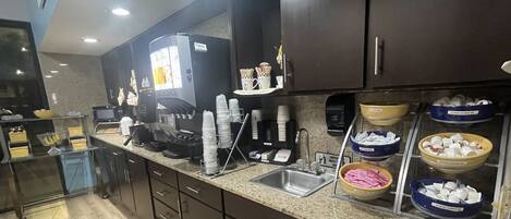 Una cocina con estación de café, un lavamanos y diferentes recipientes para alimentos.