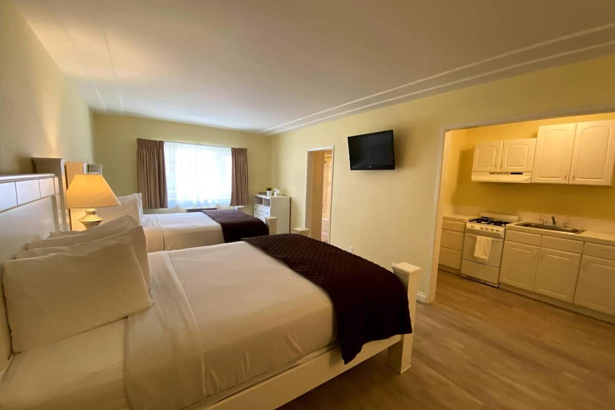 A hotel room with two beds, a TV, a desk, a window with curtains, and a kitchenette.