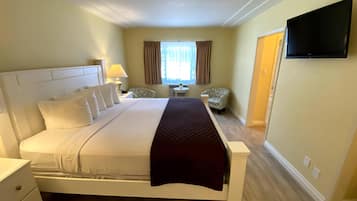 A hotel room with a large bed, a bedside table, a chair, a TV mounted on the wall, and a window with curtains.