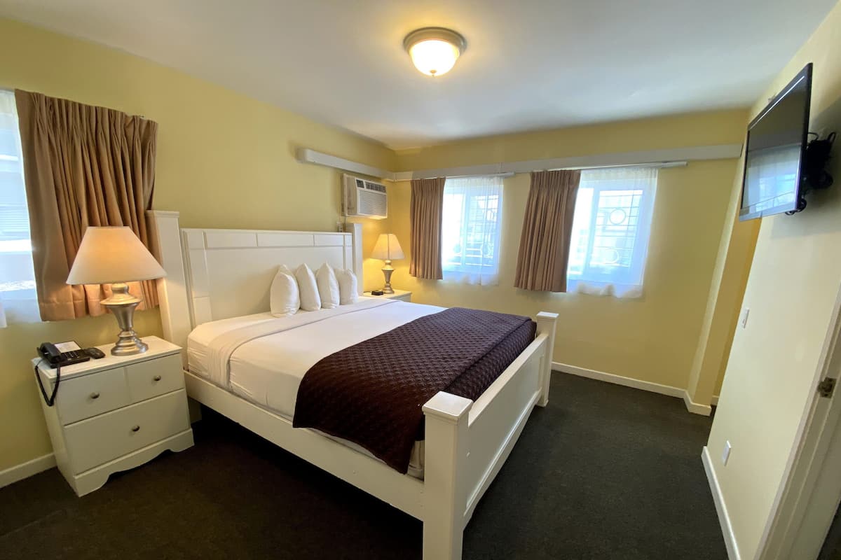 A hotel room with a bed, two bedside tables, a TV, and a window with curtains.