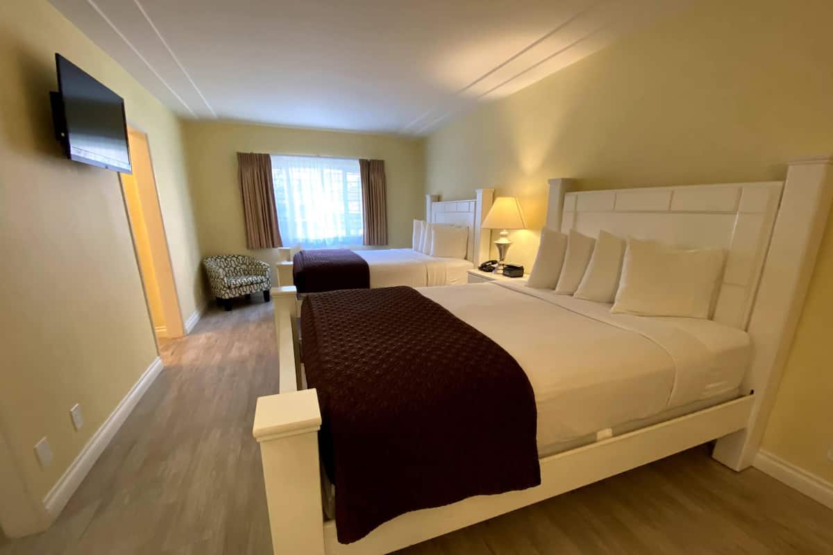 A hotel room with a large bed, a chair, a bedside table with a lamp, and a TV mounted on the wall.