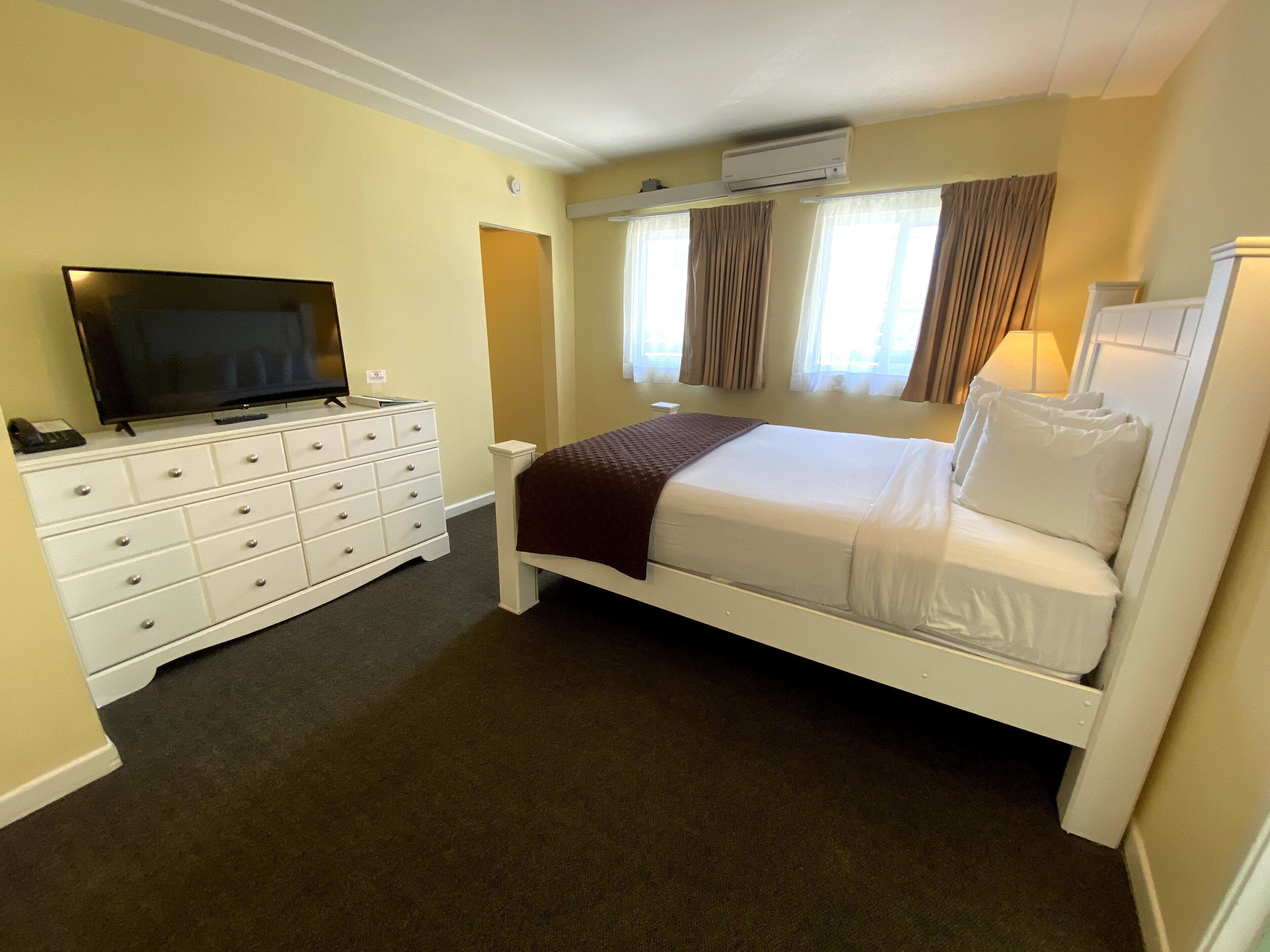 A hotel room with a bed, a dresser, a television, and an air conditioning unit.
