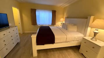 Habitación de hotel con una cama grande, dos mesitas de noche con lámparas, un televisor en una cómoda y una ventana con cortinas.