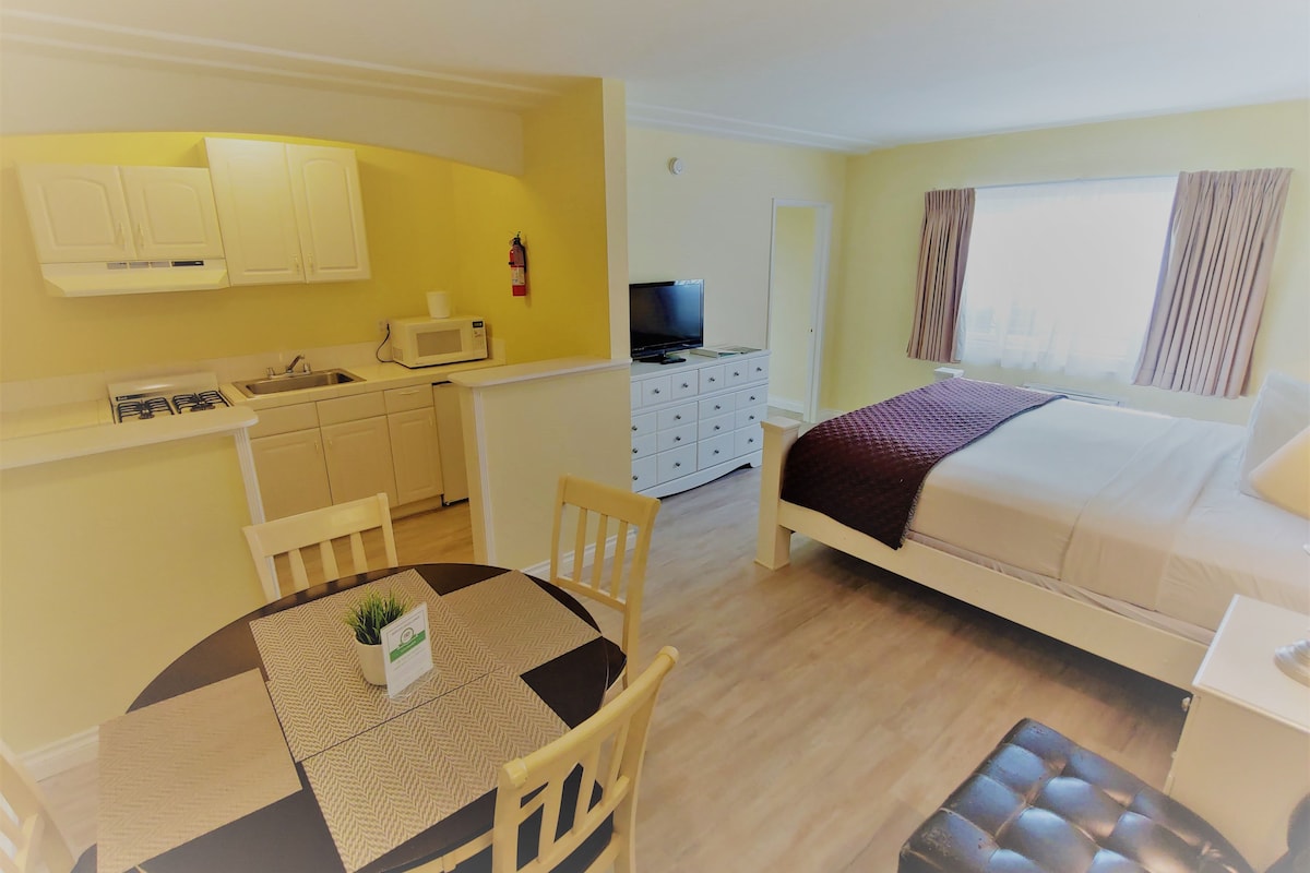 Kompakti hotellihuone, jossa on pieni keittiönurkkaus, sänky, televisio ja ikkuna, jossa on verhot.
