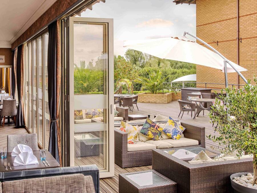 An outdoor patio with wicker furniture, a glass door leading to a garden, and a brick wall.
