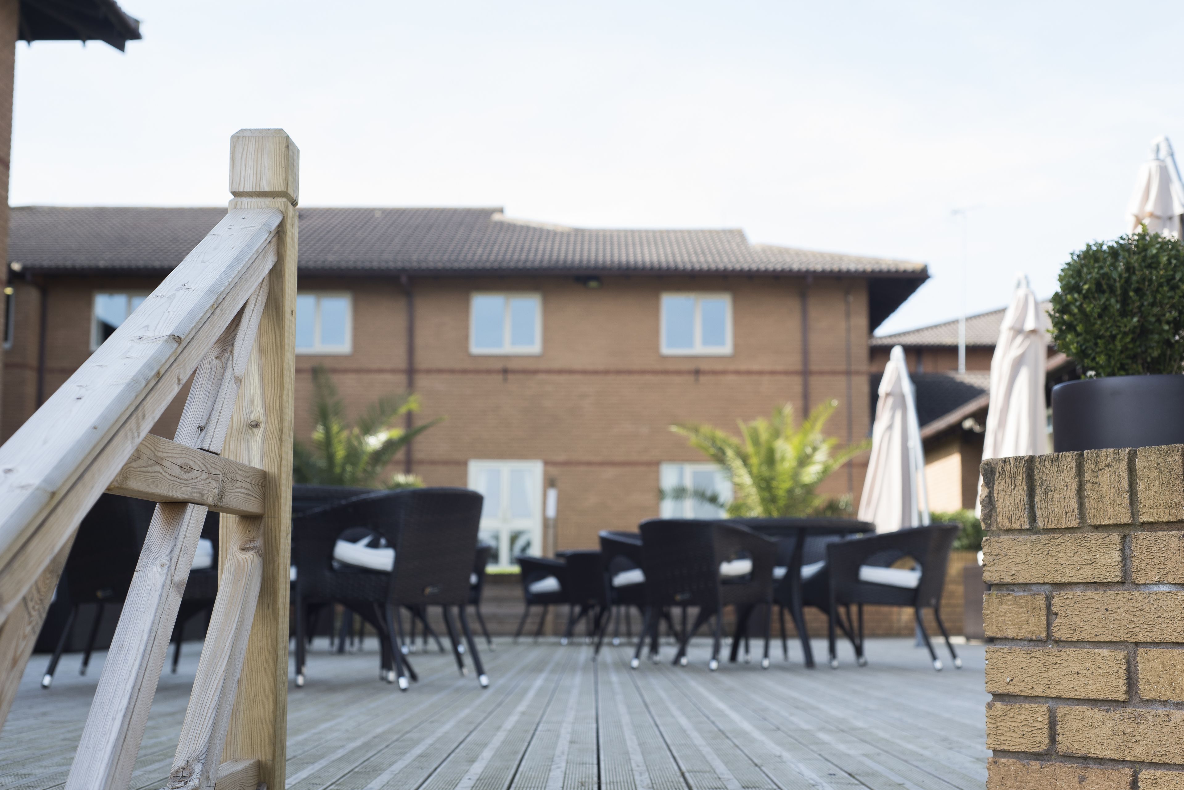 A wooden deck with outdoor seating, a brick wall, and a building with windows in the background.