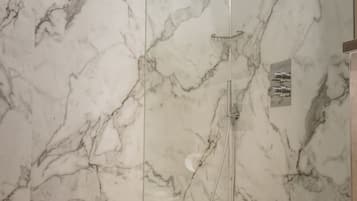 A modern bathroom with a glass-enclosed shower, marble walls, and a white sink.