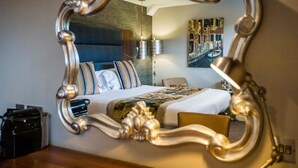 A hotel room with a large ornate mirror, a bed with a patterned bedspread, a bedside lamp, and a wall-mounted artwork. - Mercure Milton Keynes (Milton Keynes)