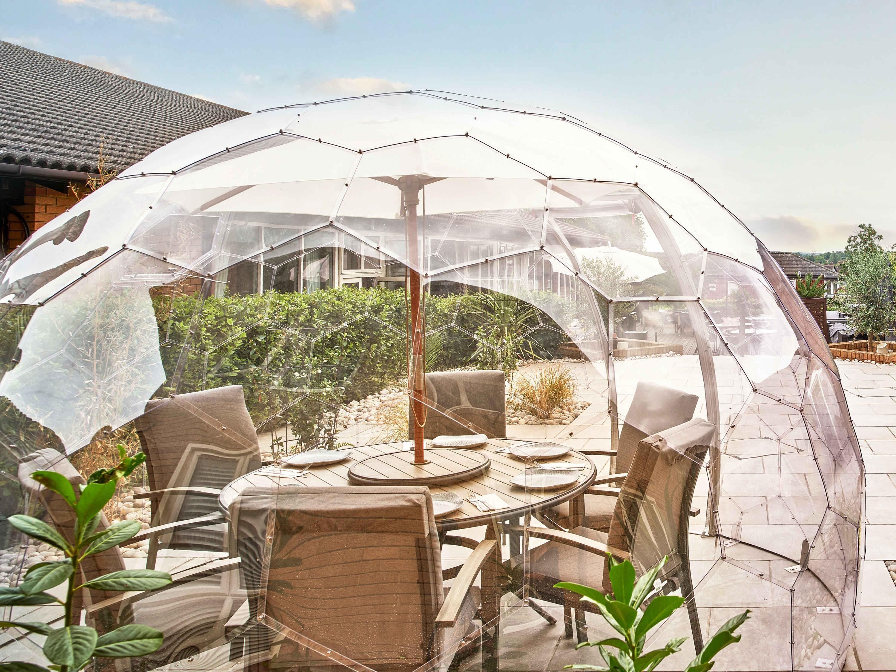 An outdoor dining area with a transparent umbrella structure, a round table, and chairs.