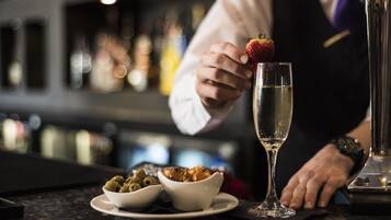 A bar setting with a bartender holding a strawberry on a glass, olives, and a bowl of food on the counter.
