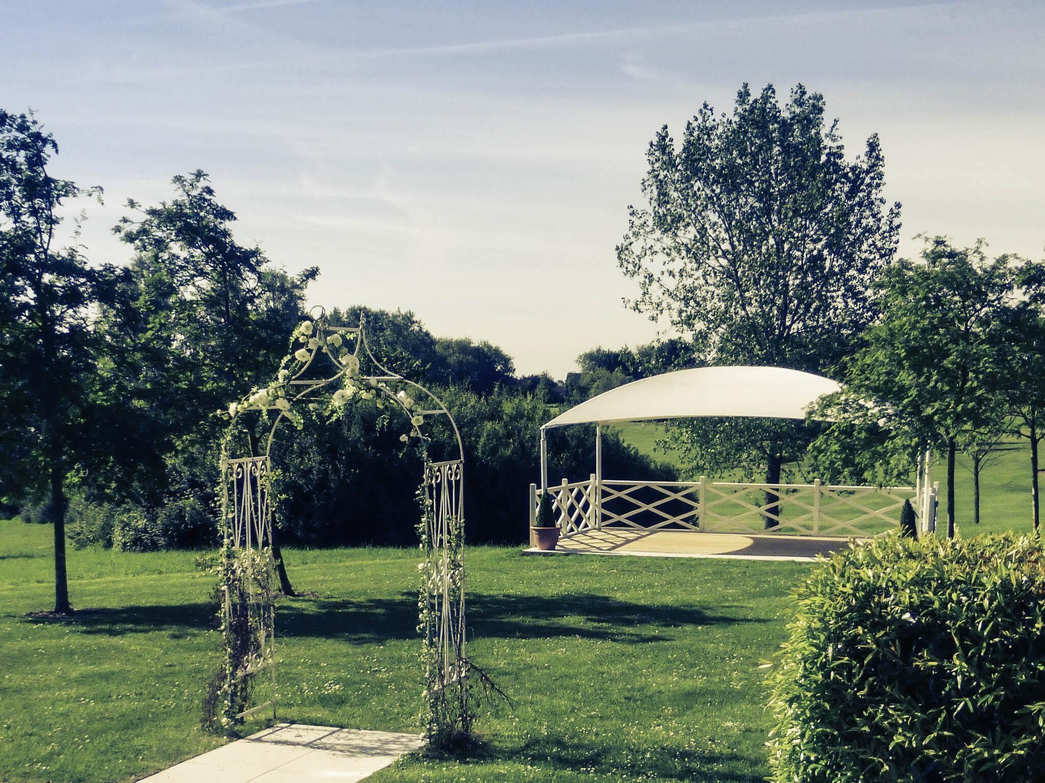 A covered outdoor area with a white canopy, surrounded by greenery and trees.