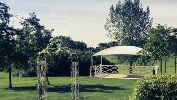 A covered outdoor area with a white canopy, surrounded by greenery and trees.