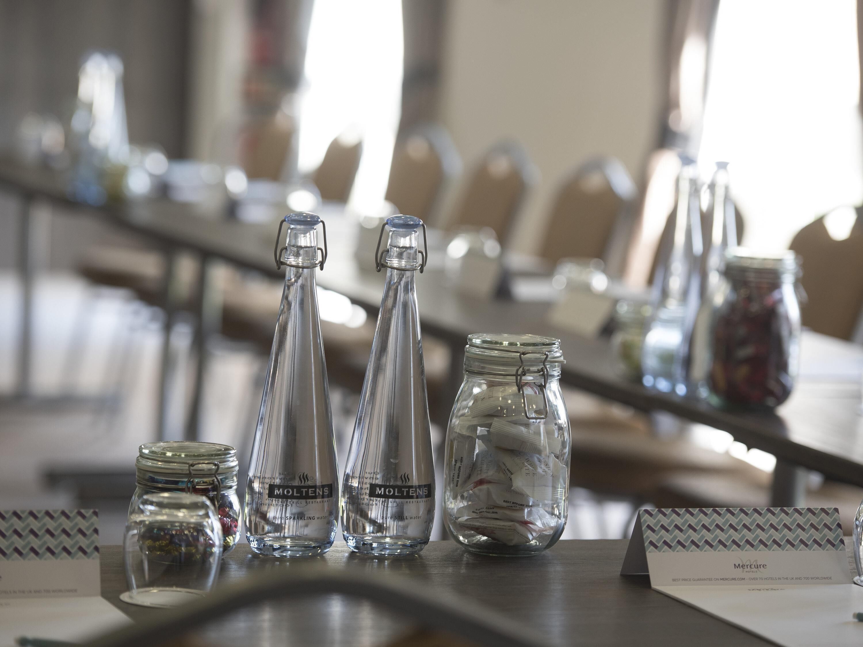 A conference table with glass bottles labeled 'Molten' and a jar filled with packets, with a sign reading 'Mercure.'